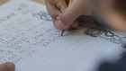 Detailausschnitt mit Fokus auf das Heft eines schreibenden Kindes