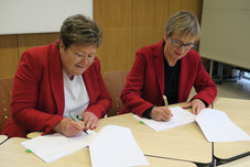 Bildungsstaatssekretärin Bettina Brück und PL-Direktorin Dr. Birgit Pikowsky unterzeichnen Dokument an Tisch sitzend