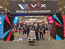 Gruppe aus Schülern und zwei Lehrkräften vor einem Rundbogen mit Schrift VEX World Championship
